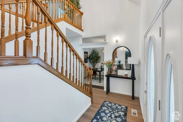 Two-story foyer with wood-finish flooring, a grand staircase with wood balusters, and a decorative wall sconce