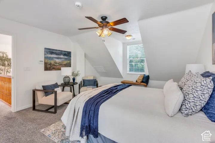 Sloped ceilings, window with blinds, ceiling fan with light fixture, carpeted flooring, and built-in window bench