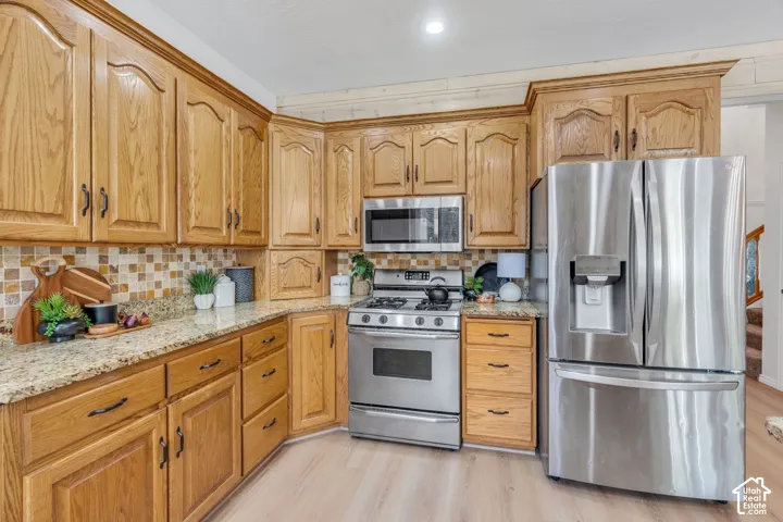 Kitchen featuring wood cabinetry, stainless steel appliances, mosaic tile backsplash, granite countertops, and wood-finish flooring
