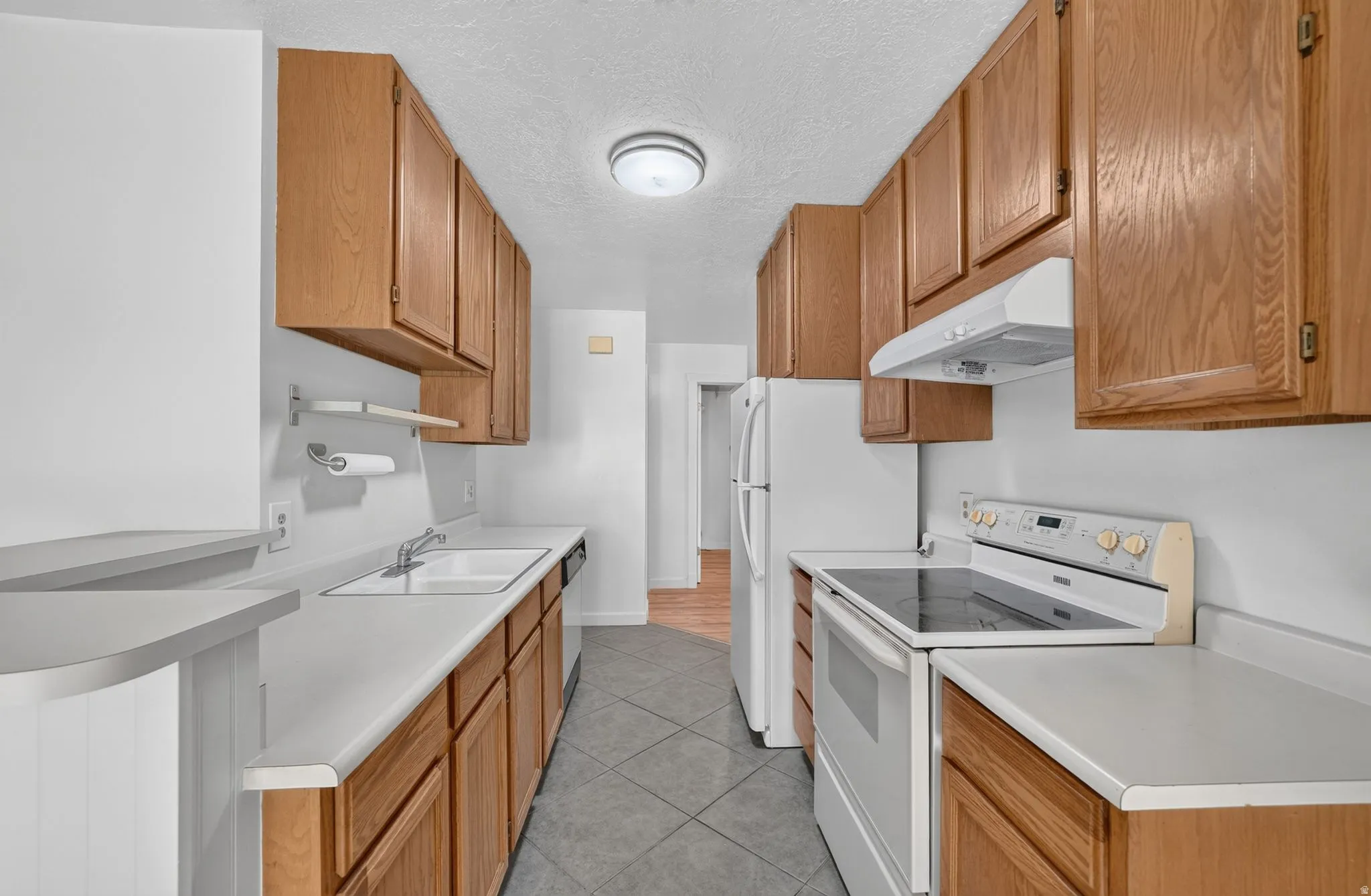 Galley kitchen featuring wood cabinetry, white appliances, and a built-in breakfast bar