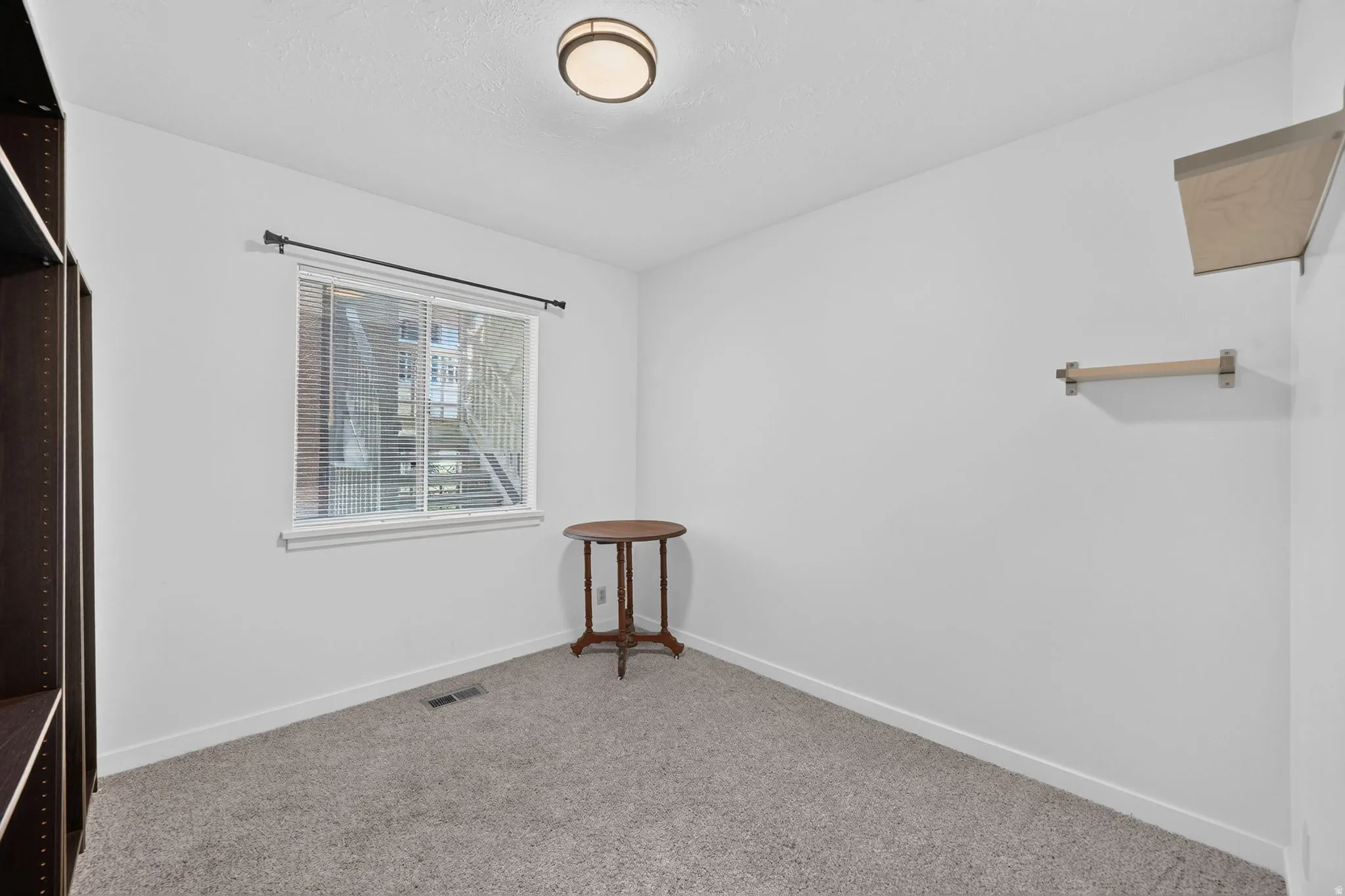 Recessed window with blinds, overhead flush mount light fixture, and wall-mounted shelving