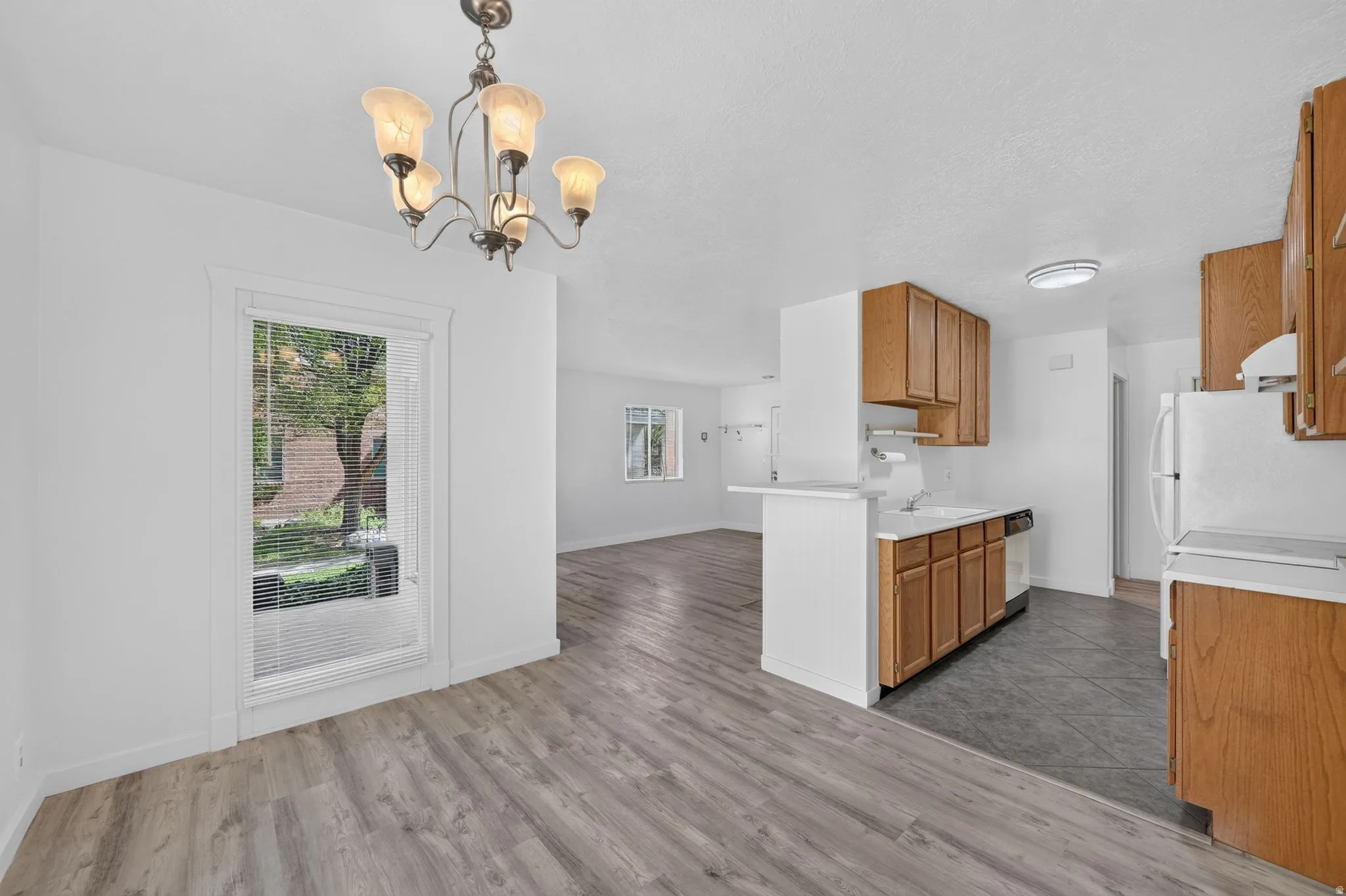 Open-concept living space with wood-finish flooring, a kitchen featuring wood cabinetry and white countertops, and a dining area with an overhead chandelier