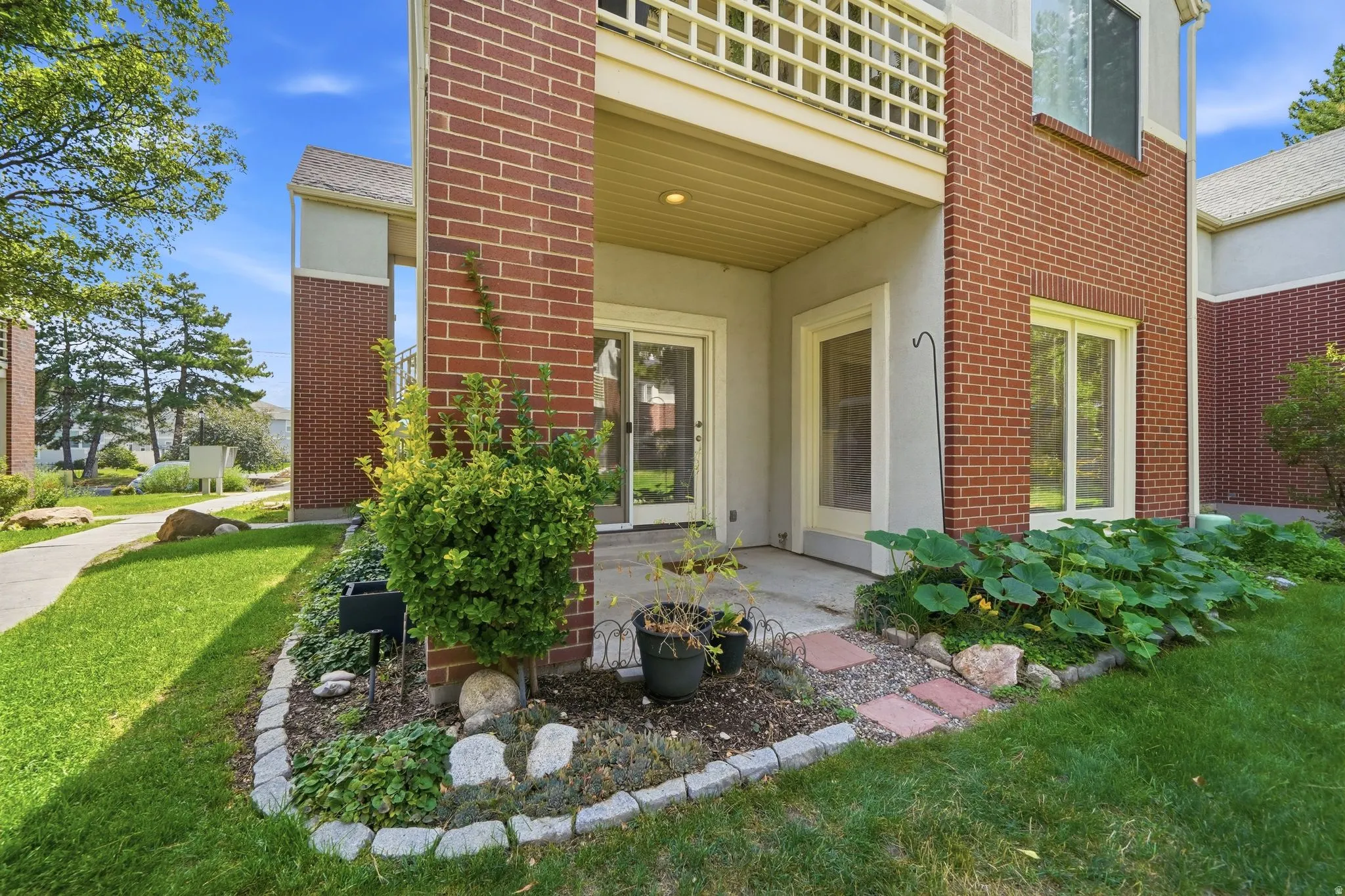 Exterior brick and stucco facade with a ground-level patio, a dedicated garden bed, and a landscaped lawn area