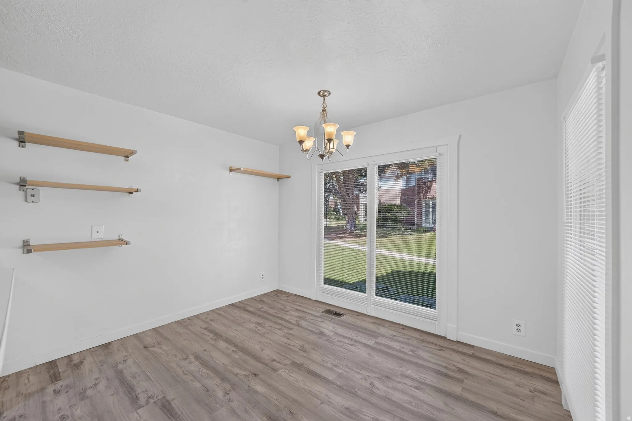 Wood-finish flooring, white walls, built-in shelving, glass sliding door, and a chandelier fixture