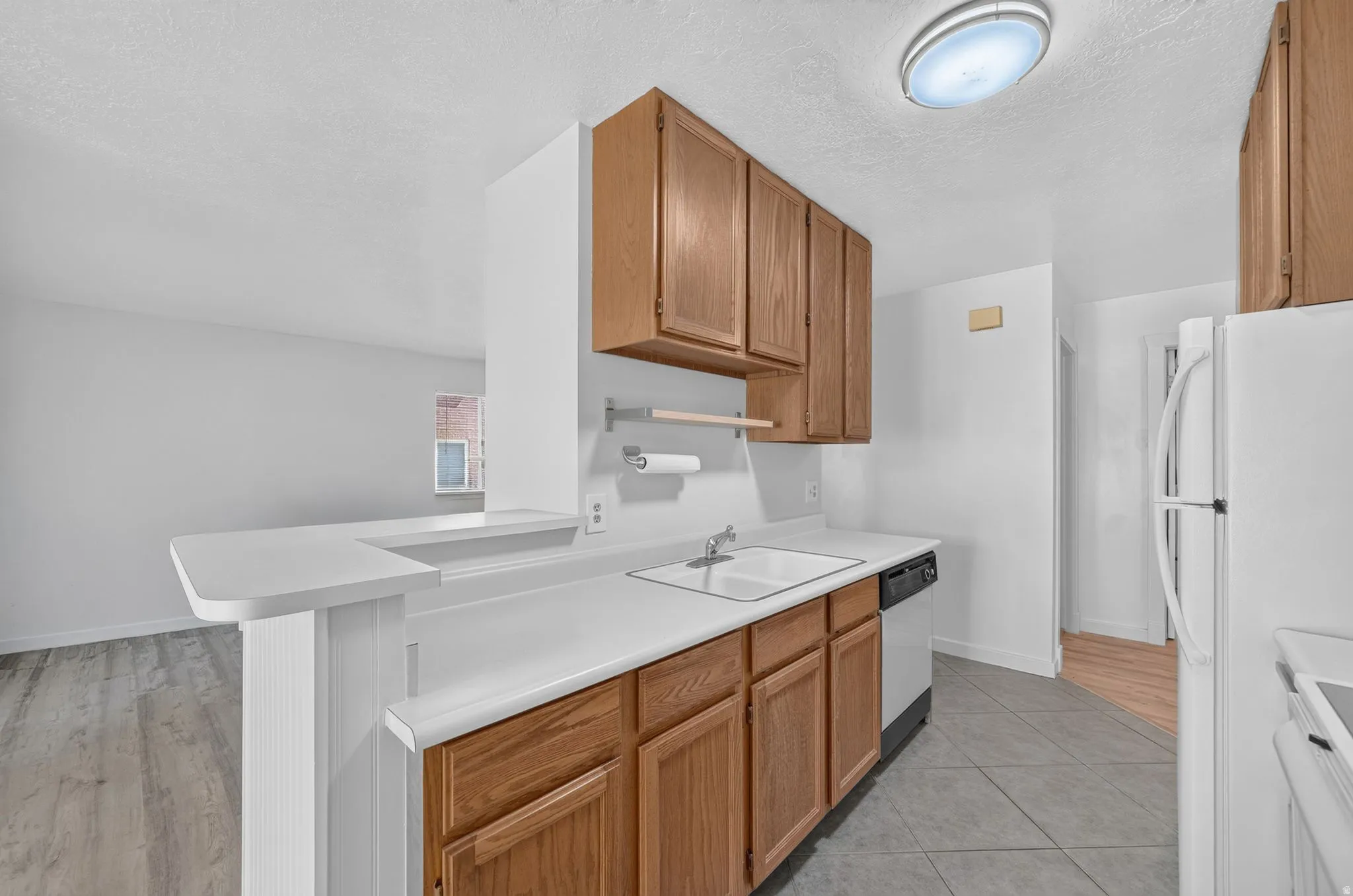 Kitchen featuring wood-finish cabinetry, white countertops, a drop-in sink, and tile flooring