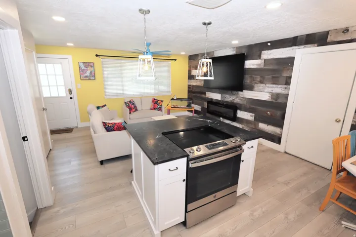 Kitchen island with integrated stainless steel range, light wood-finish flooring, recessed ceiling lighting, and a wood plank accent wall