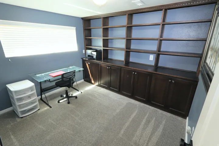 Built-in shelving and cabinetry with dark wood-finish, wall-to-wall carpeting, and a window with horizontal blinds