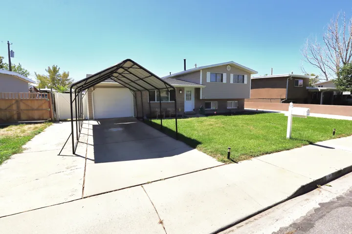Split-level residence featuring a front lawn, paved driveway, attached single-car garage, and a carport structure