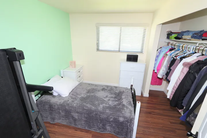 Wood-finish flooring, a window with horizontal blinds, and a built-in closet with shelving and hanging rods