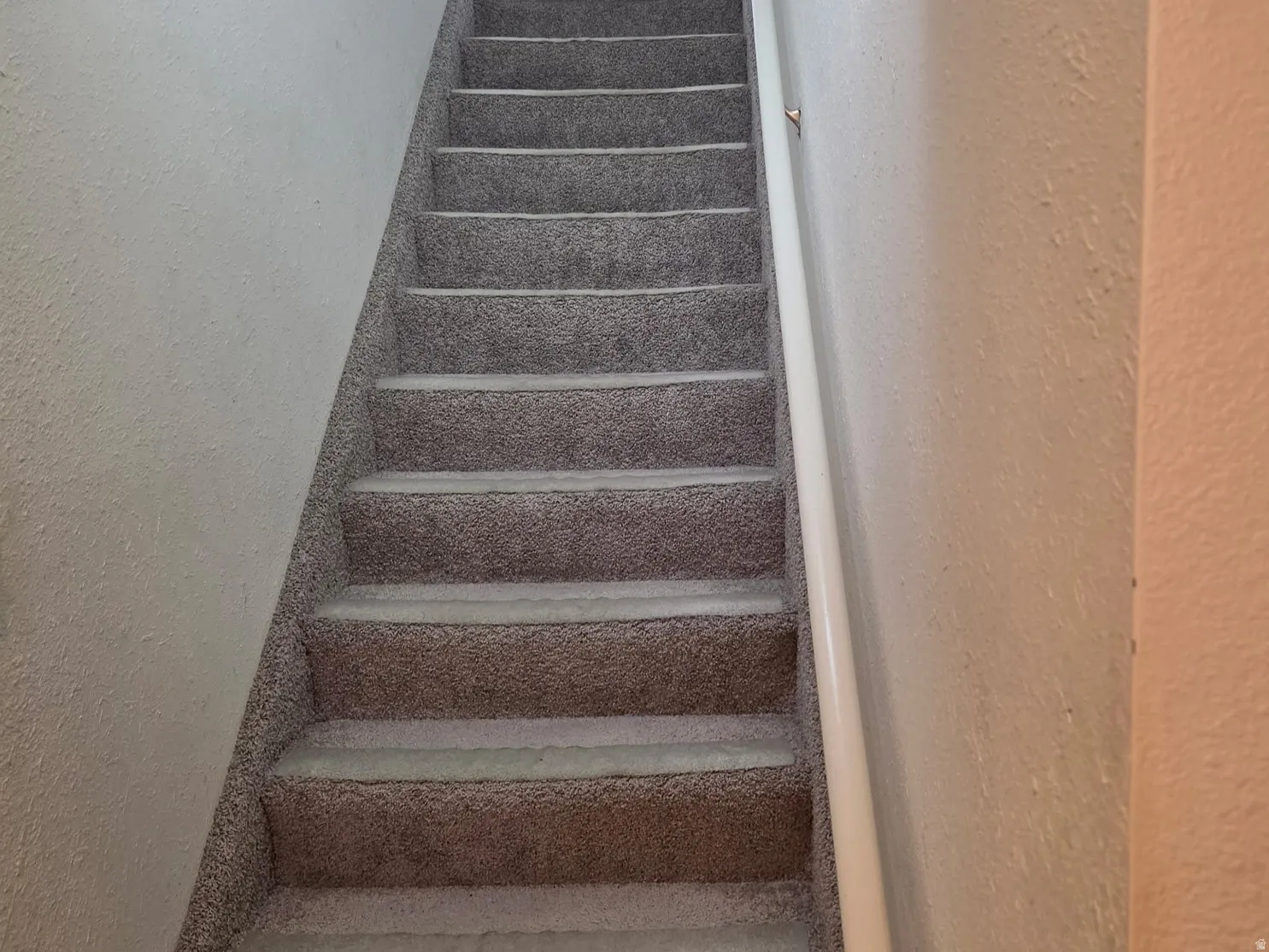 Carpeted staircase with a wall-mounted handrail leading to a white door