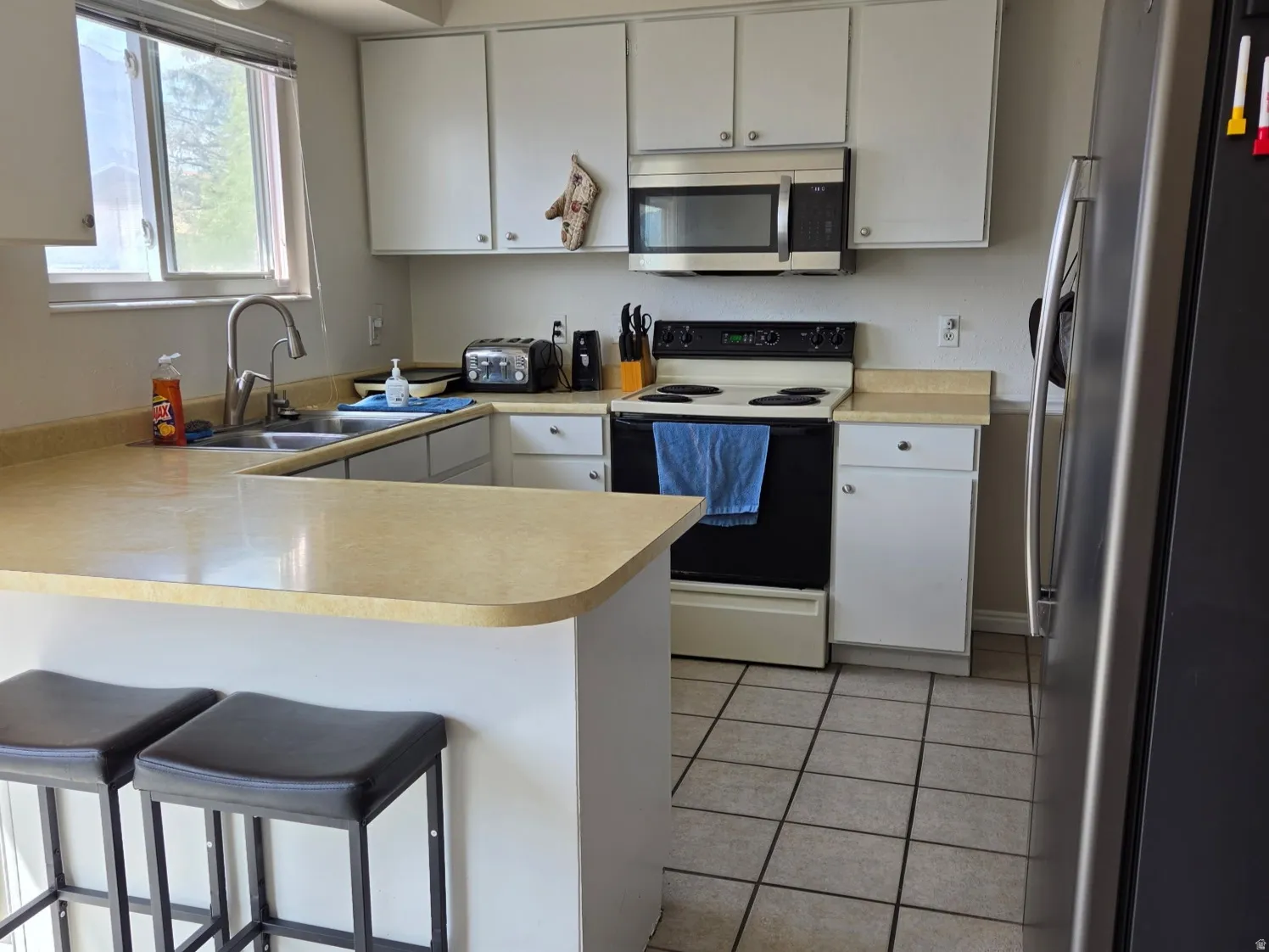 Kitchen featuring white cabinetry, light-toned countertops, a stainless steel refrigerator, and tiled flooring
