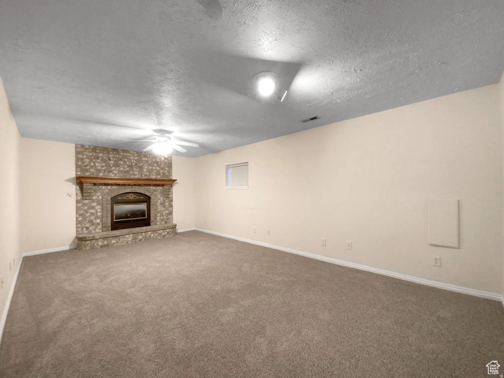 Previous picture Spacious room featuring a stone-faced fireplace with a wood mantle, neutral wall paint, ceiling fan, and carpet flooring