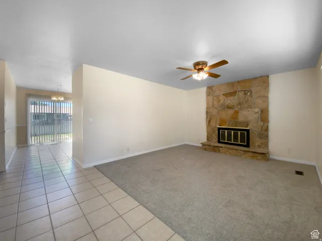 Previous picture Stone-clad fireplace with a metal insert, ceiling fan with integrated lighting, tiled flooring, and carpeted flooring