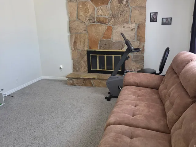 Stone-clad fireplace with hearth, wall-to-wall carpeting, and a ceiling fan with integrated lighting