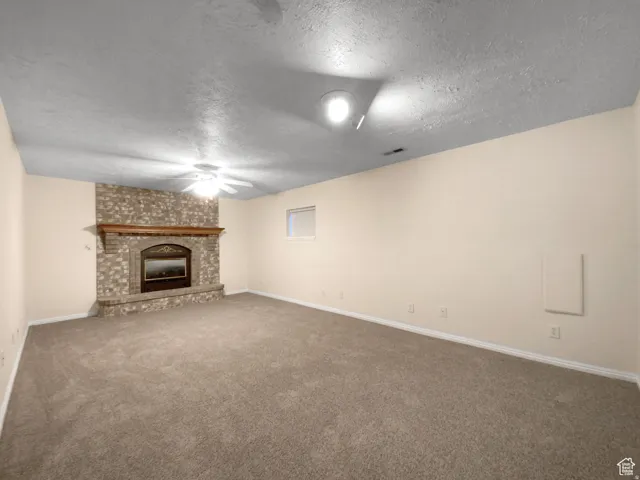 Previous picture Spacious room featuring a stone-faced fireplace with a wood mantle, neutral wall paint, ceiling fan, and carpet flooring
