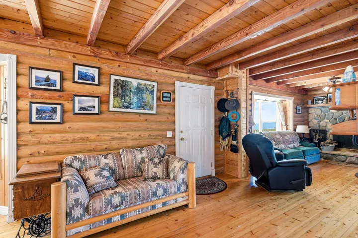 Exposed wood beam ceiling, wood-paneled walls, wood-finish flooring, white paneled interior door, stone-clad fireplace