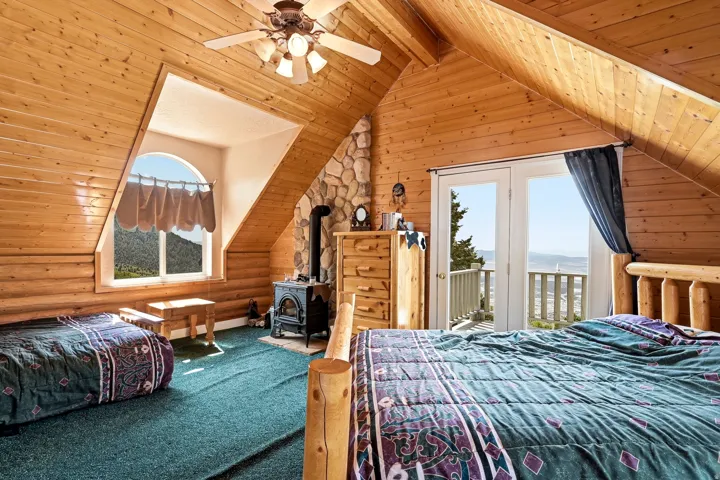 Sloped wood-paneled ceilings, wood-plank walls, stone-surround fireplace, arched window, and double glass doors opening to a balcony