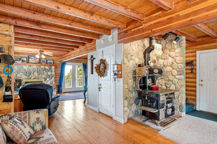 Exposed wood beam ceiling, hardwood flooring, stone accent wall, stone fireplace, and double French doors