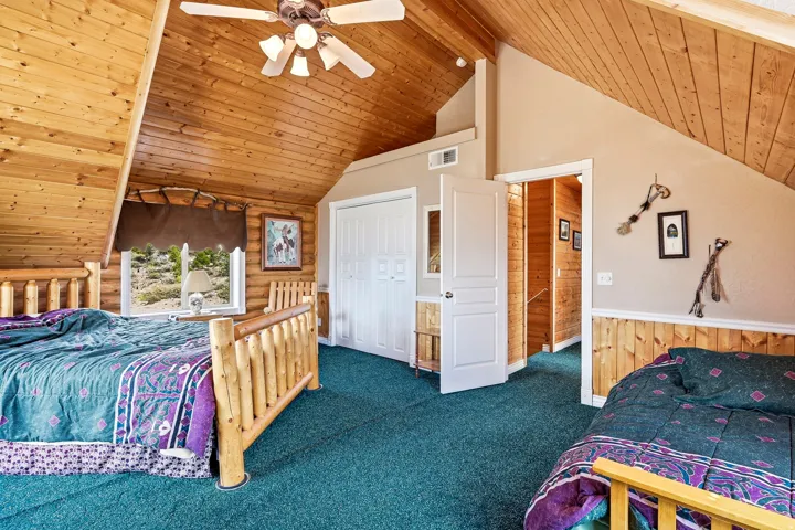 Sloped wood-paneled ceiling, wood-paneled accent wall, neutral wall paint, ceiling fan with integrated lighting, and a window with exterior scenery