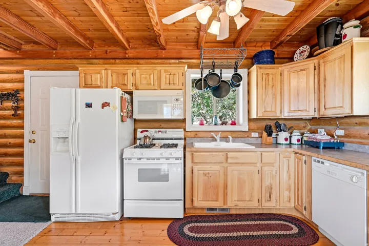Wood-finish flooring, exposed wood beam ceiling, wood cabinetry, white appliances, and a ceiling fan