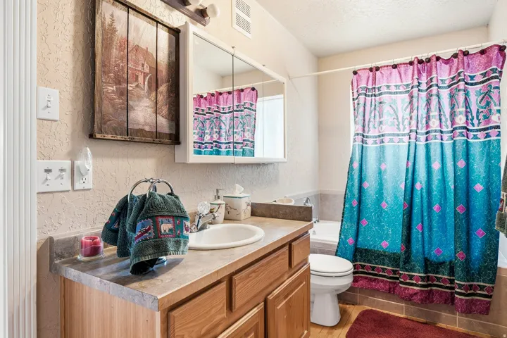 Full bathroom featuring a wood-finish vanity with dual-basin sink, stone countertop, and ceramic tile flooring