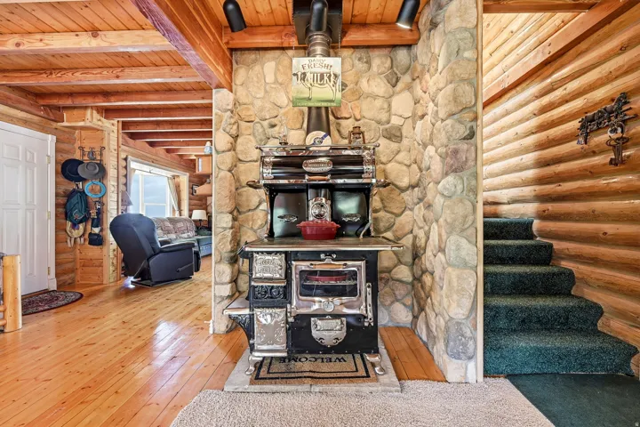 Wood-paneled ceilings with exposed beams, wood-finish flooring, stone-clad wall, built-in black stove, and wood-paneled walls