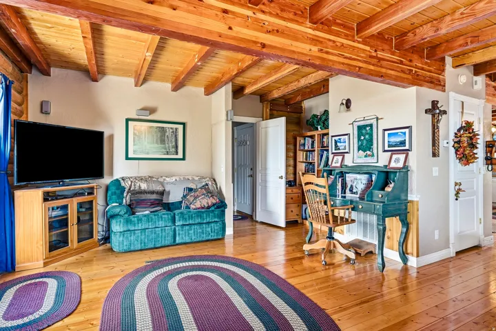 Open-concept living area featuring exposed wood beam ceiling, hardwood flooring throughout, and abundant natural light
