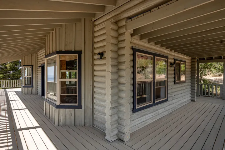 Expansive covered porch featuring wood flooring and railings, bay windows, and log-style exterior siding