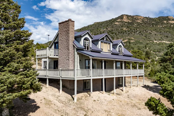 Log-style exterior featuring a stone chimney, multiple dormer windows, and a wrap-around porch