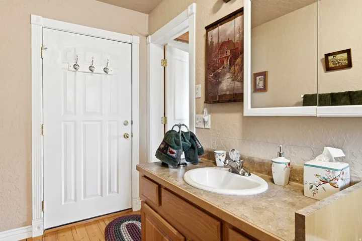 Recessed-panel door with brass hardware, wood-finish flooring, and a vanity with a drop-in sink