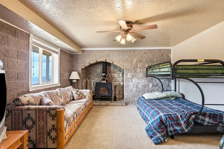 Stone block wall details, wood-burning stove, archway fireplace surround, ceiling fan with integrated lighting, carpeted flooring