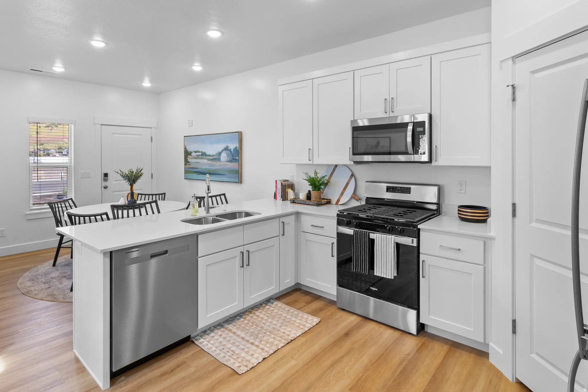 Modern kitchen featuring white shaker cabinetry, stainless steel appliances, light-toned countertops, and wood-finish flooring