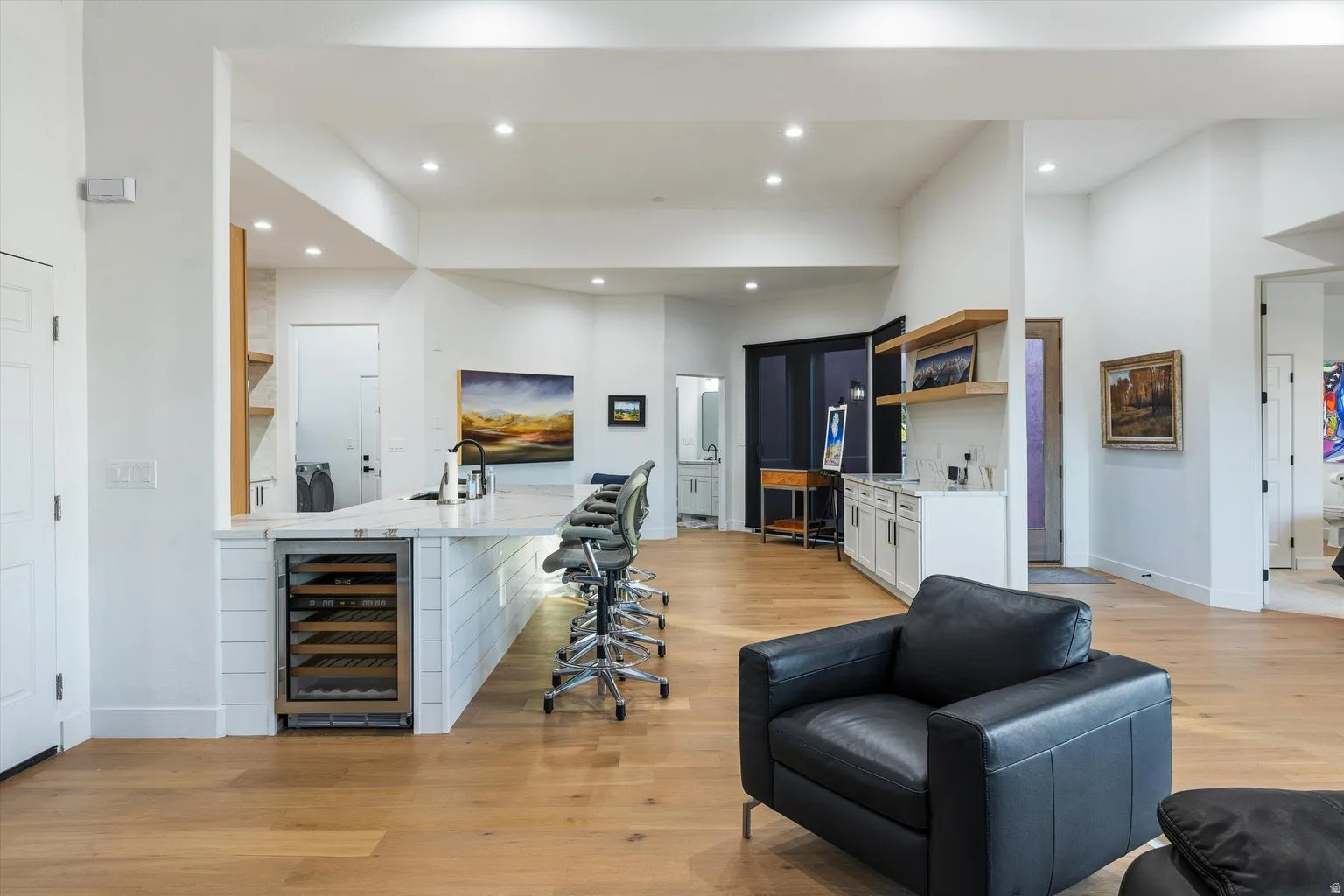 Open-concept living area with wood-finish flooring, a kitchen island featuring a beverage cooler, recessed lighting, and a built-in wet bar with floating shelves