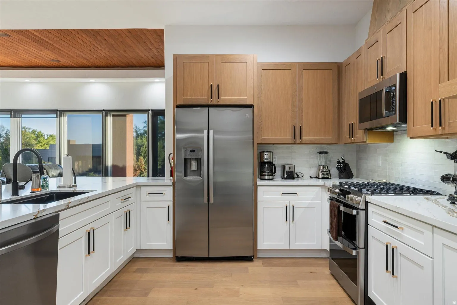 Kitchen featuring wood-finish flooring, two-tone cabinetry, stainless steel appliances, a tile backsplash, and stone countertops