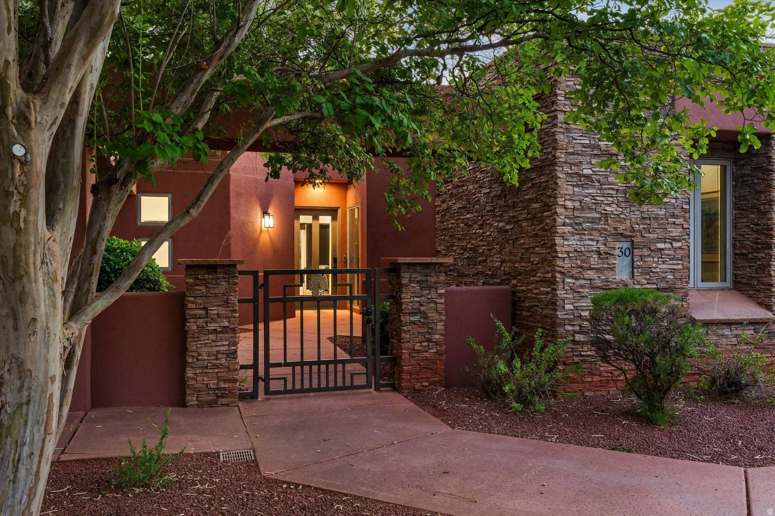 Stucco exterior with stone veneer accents, decorative wrought iron gate, and mature landscaping