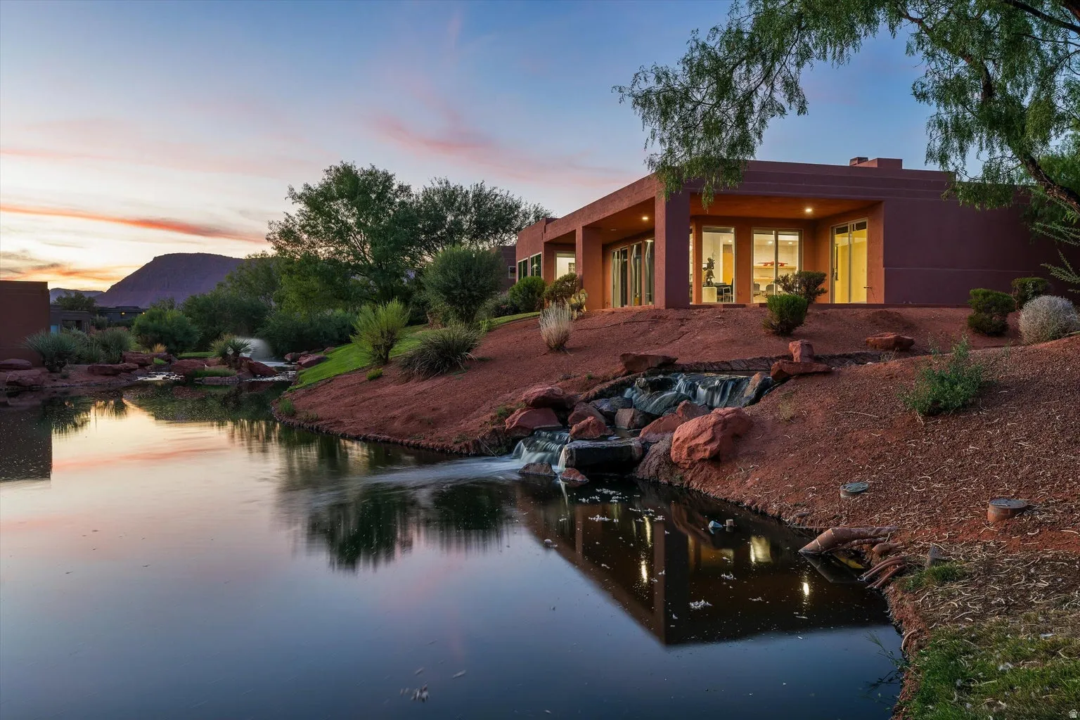Contemporary exterior with expansive windows, surrounded by a pond and natural landscaping, featuring a cascading waterfall