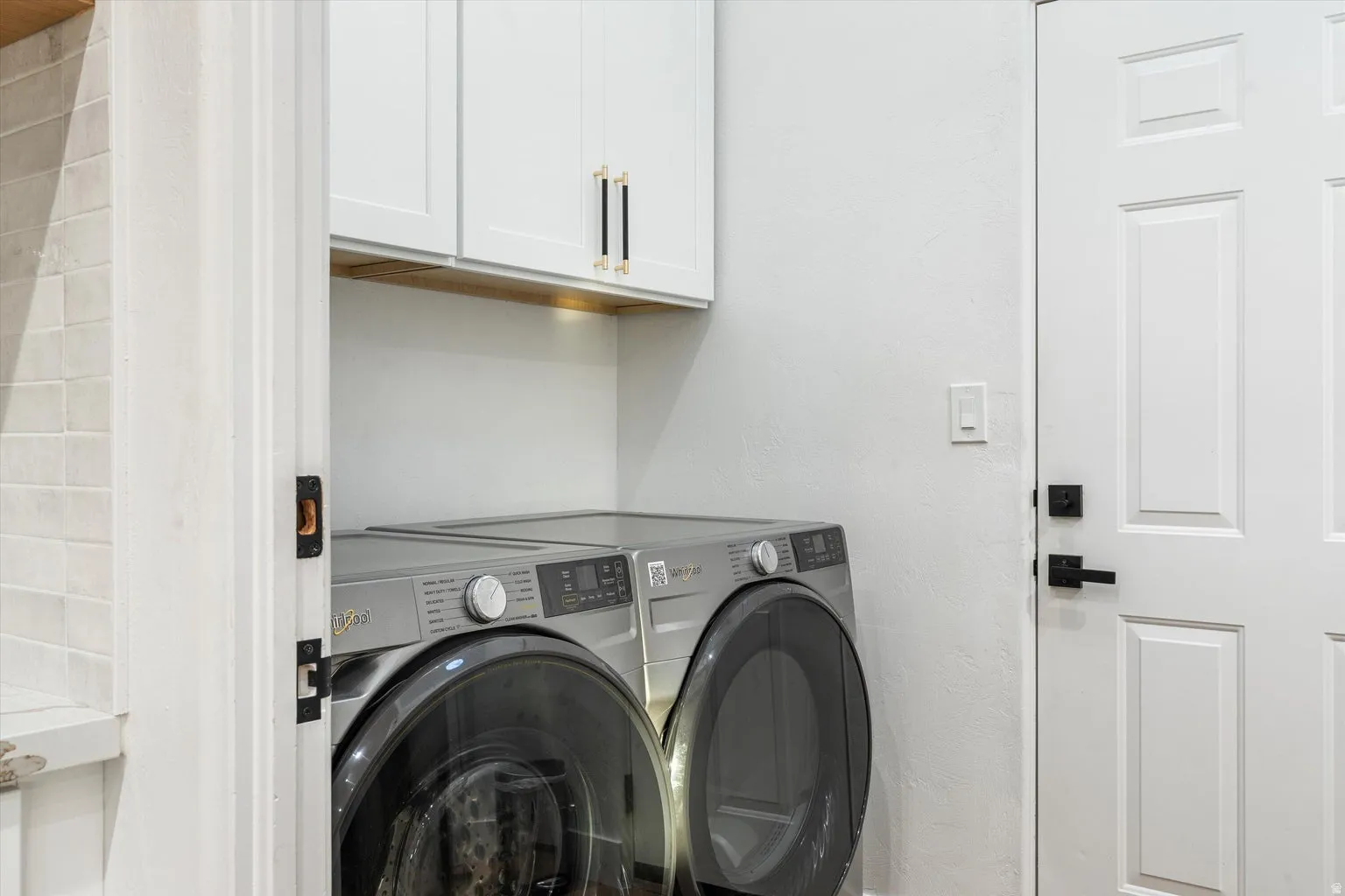 Built-in white cabinetry with gold and black hardware, wood-finish accent shelving, and a paneled door with matte black hardware