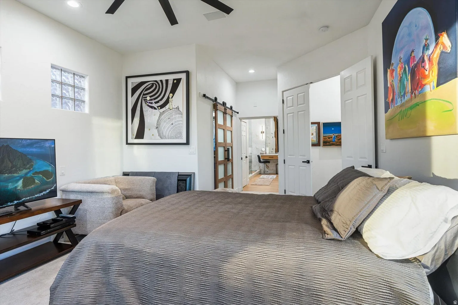 Vaulted ceiling, ceiling fan, glass block window, wood-finish sliding barn door, and hard surface flooring