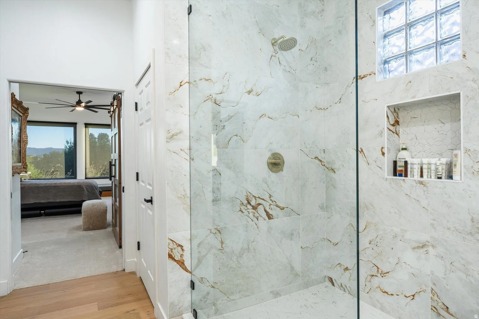 Glass-enclosed shower with large format marble-look tile, rainfall showerhead, and integrated niche