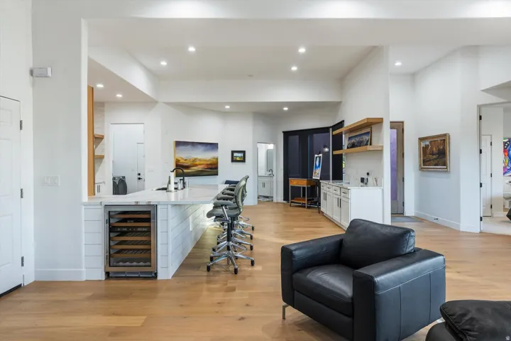 Open-concept living area with wood-finish flooring, a kitchen island featuring a beverage cooler, recessed lighting, and a built-in wet bar with floating shelves