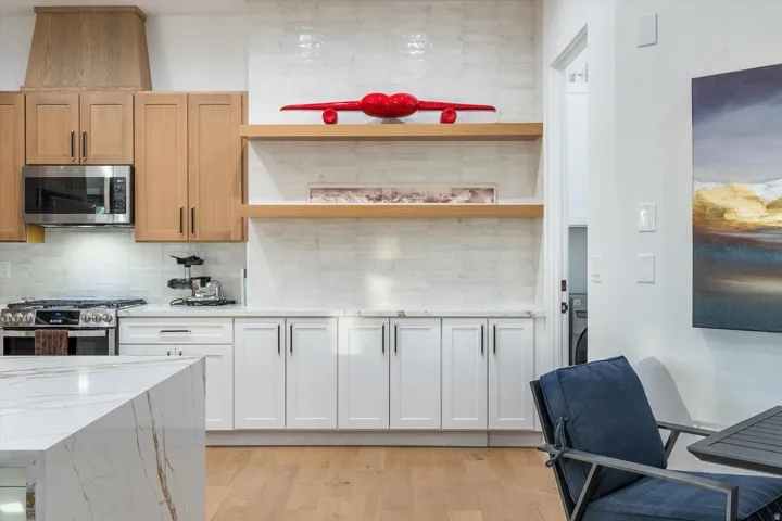 Wood-finish flooring, white countertops, built-in stainless steel microwave, wood-finish upper cabinetry, white lower cabinetry