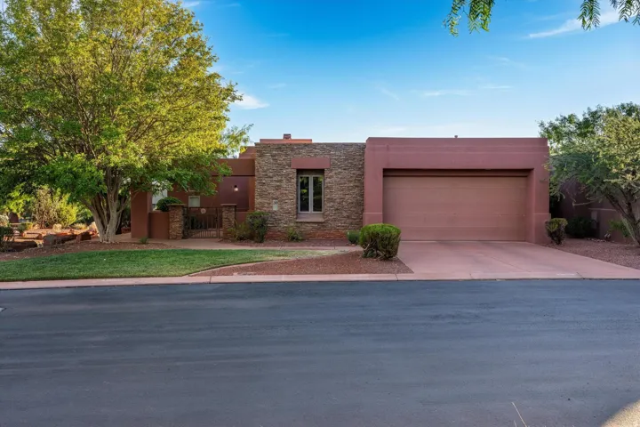 Stucco exterior with stone accents, integrated garage, paved driveway, mature landscaping, and decorative metal gate