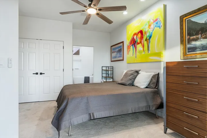 Recessed lighting, ceiling fan with light fixture, carpeted flooring, white paneled doors with black hardware, and an adjacent bathroom space
