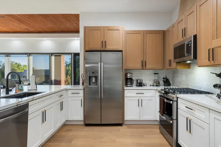 Kitchen featuring wood-finish flooring, two-tone cabinetry, stainless steel appliances, a tile backsplash, and stone countertops