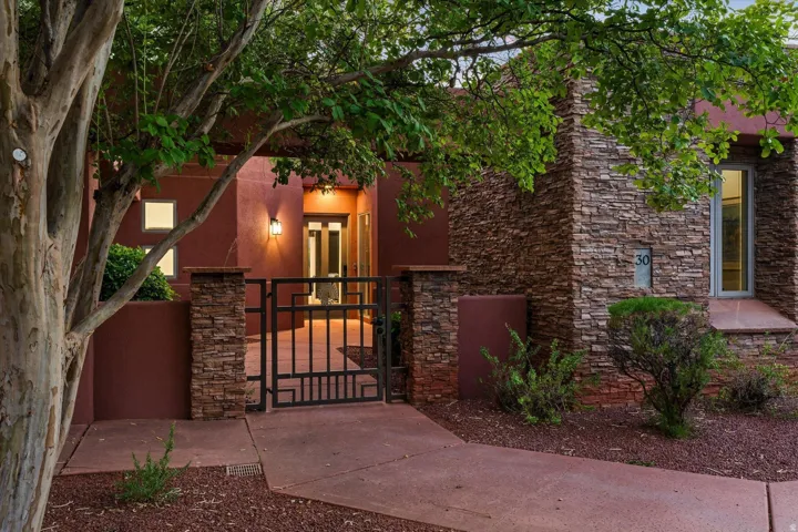 Stucco exterior with stone veneer accents, decorative wrought iron gate, and mature landscaping