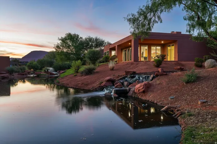 Contemporary exterior with expansive windows, surrounded by a pond and natural landscaping, featuring a cascading waterfall
