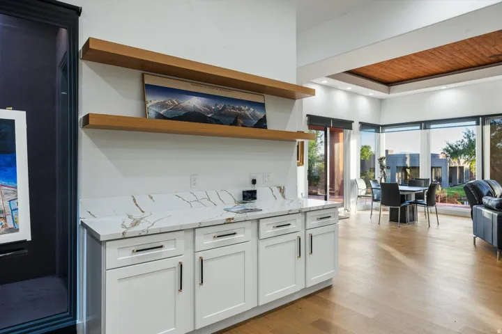 White cabinetry with dark hardware, stone-finish countertop, and floating wood shelves