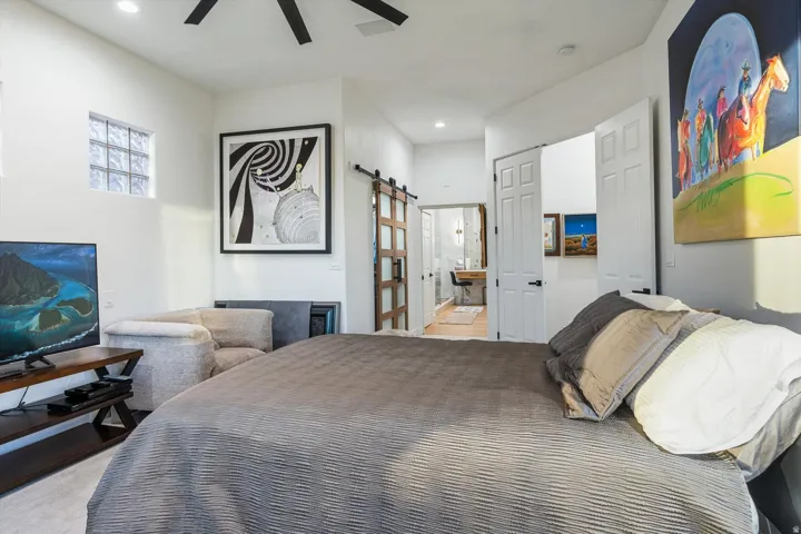 Vaulted ceiling, ceiling fan, glass block window, wood-finish sliding barn door, and hard surface flooring