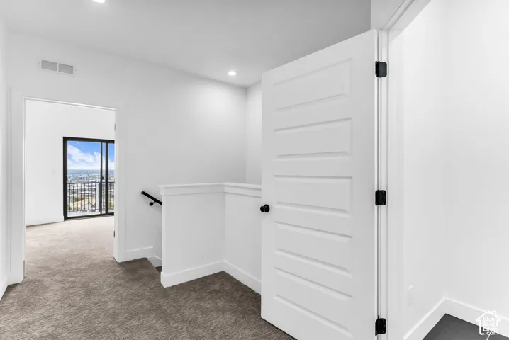 Carpeted hallway with white walls, recessed lighting, and white paneled doors with black hardware