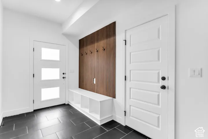 Bright entryway showcasing slate-finish tile flooring, white shaker-style doors with black hardware, a dark wood-finish accent wall with vertical paneling and wall-mounted hooks, and recessed ceiling lighting throughout
